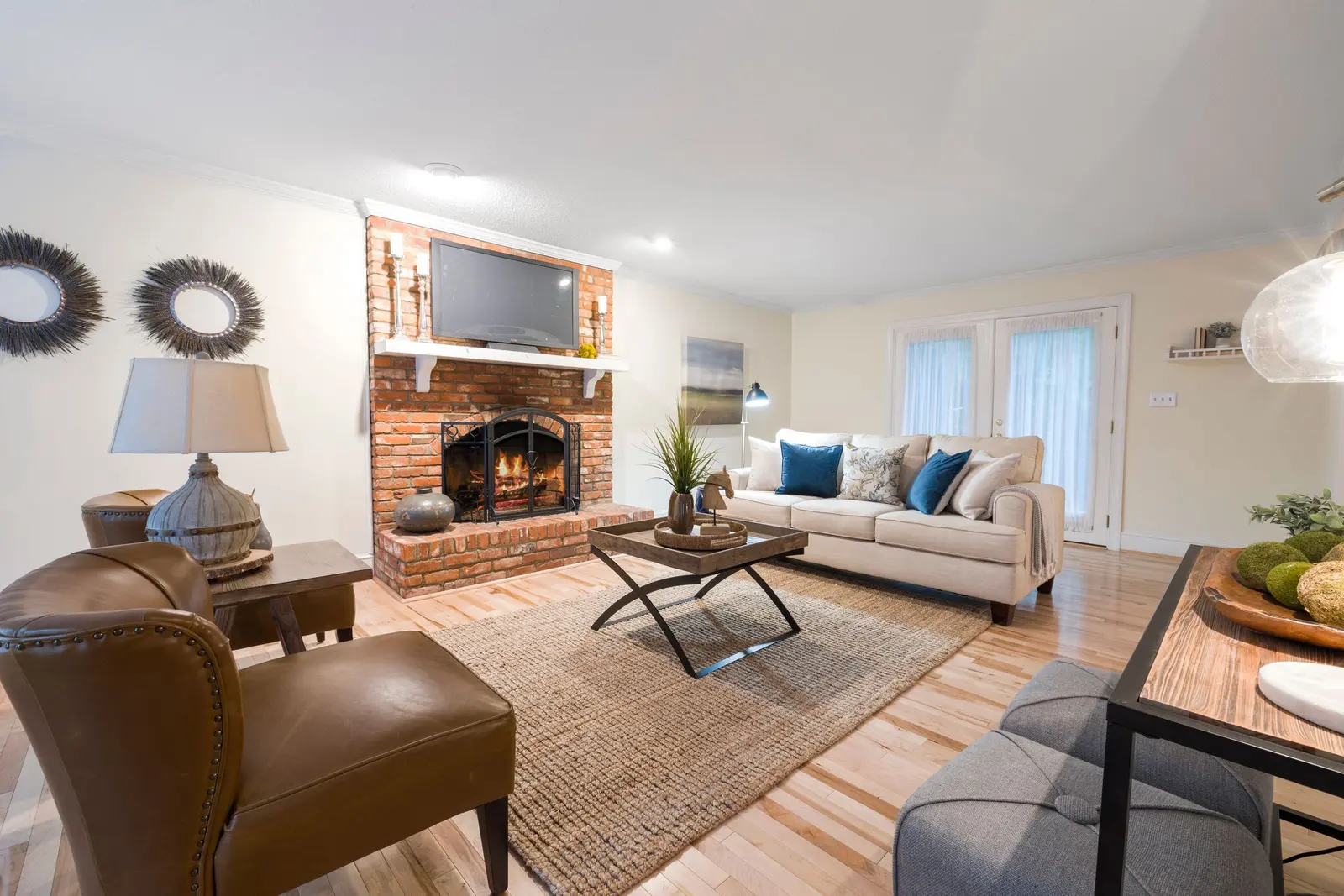 Light wood floor in a living room with a brick fireplace, leather chairs and a patterned rug