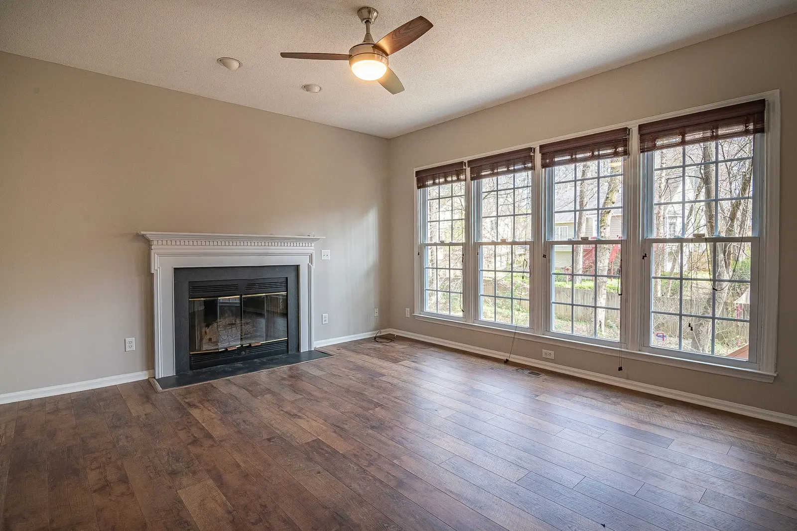 Dark-stained hardwood floor in a living room with a white fireplace and a wall of windows