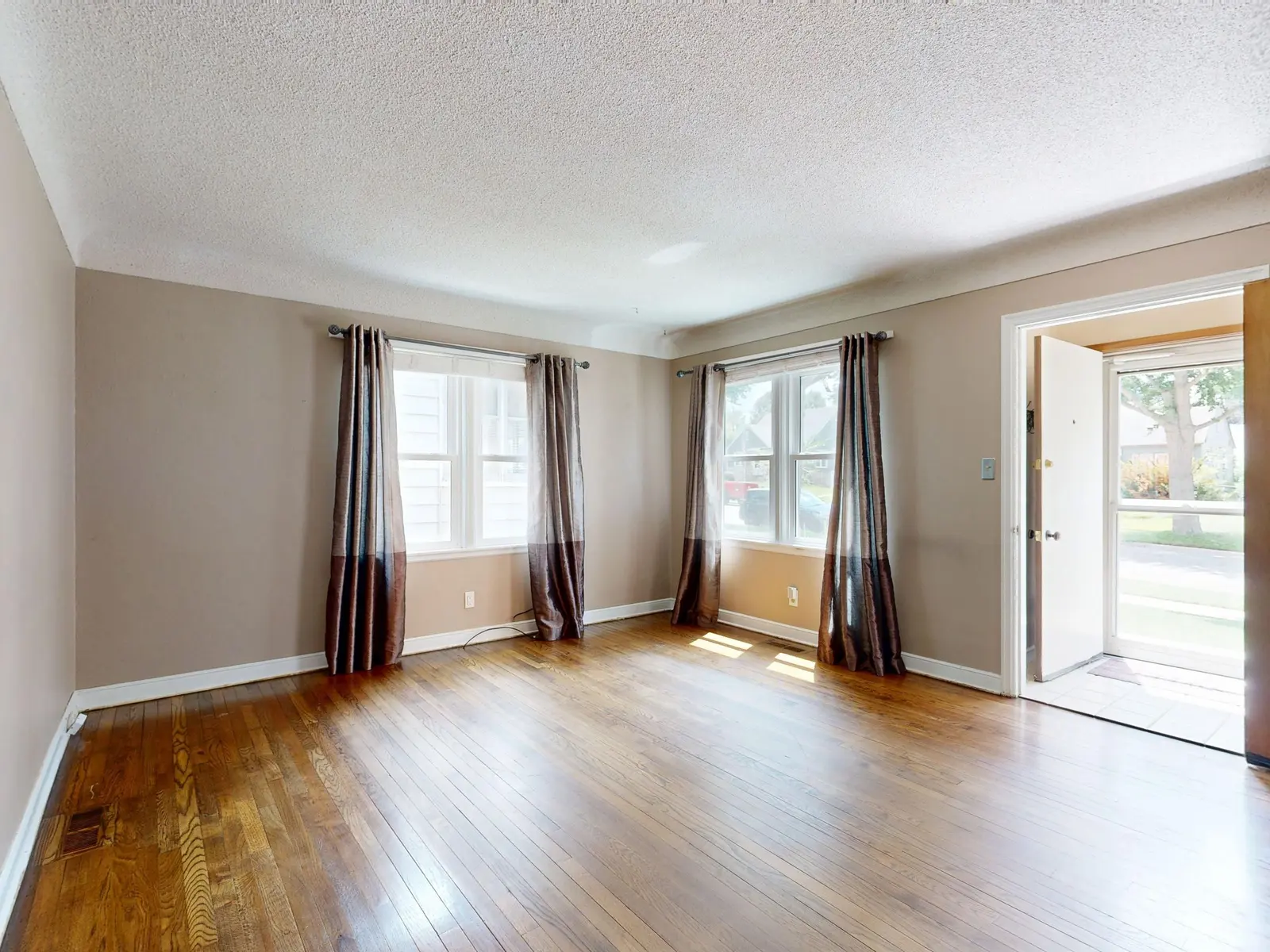 Red oak hardwood in an empty room with floor-length curtains and an open exterior door