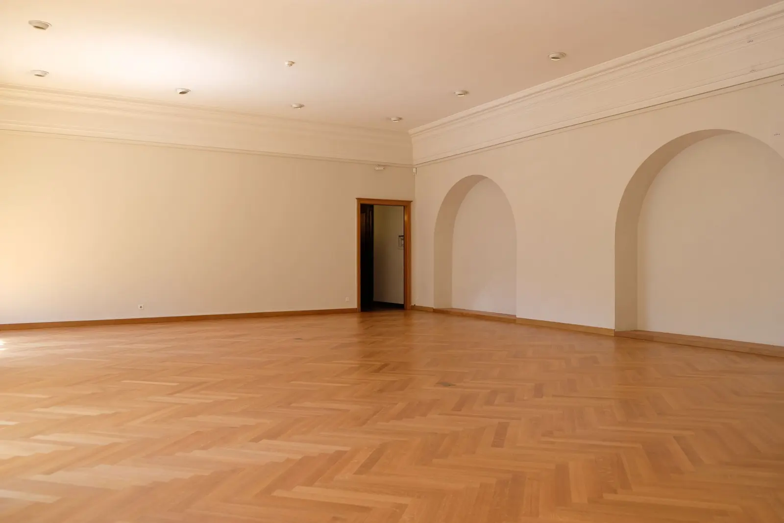 Light oak herringbone floor filling a large empty room with arched doorways and crown molding