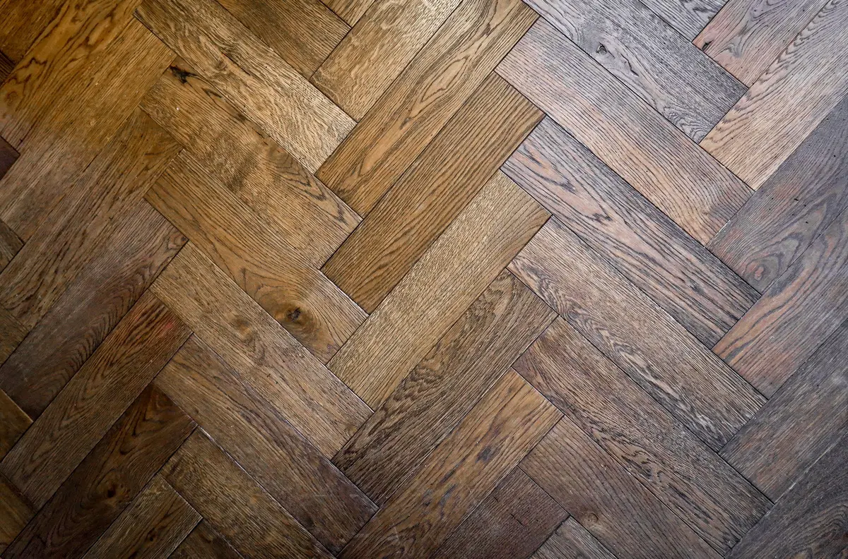 Close-up of a rustic herringbone parquet floor showing heavy grain and knots in the oak
