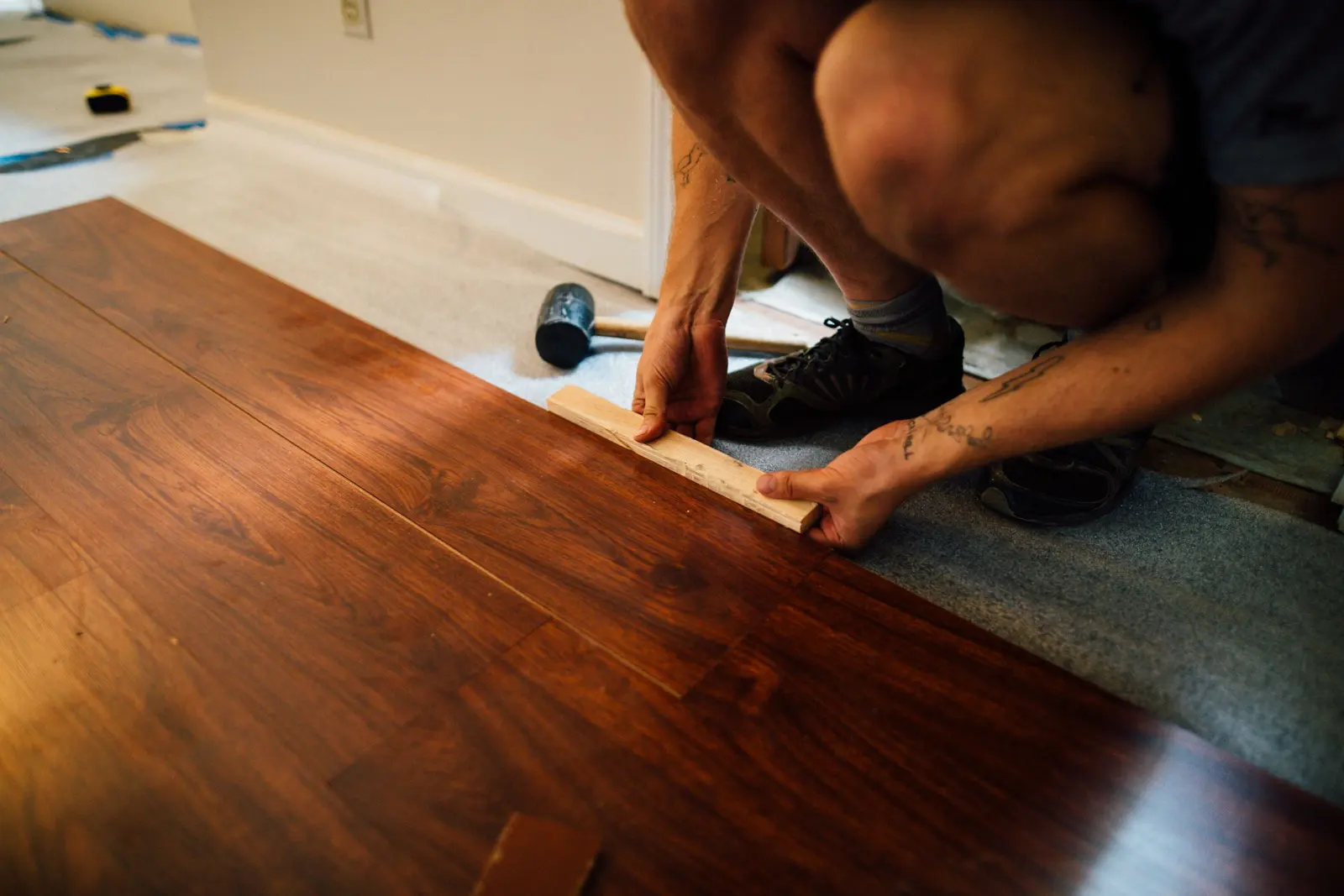 Installer tapping a dark wood-grain plank into place with a mallet over fresh underlayment