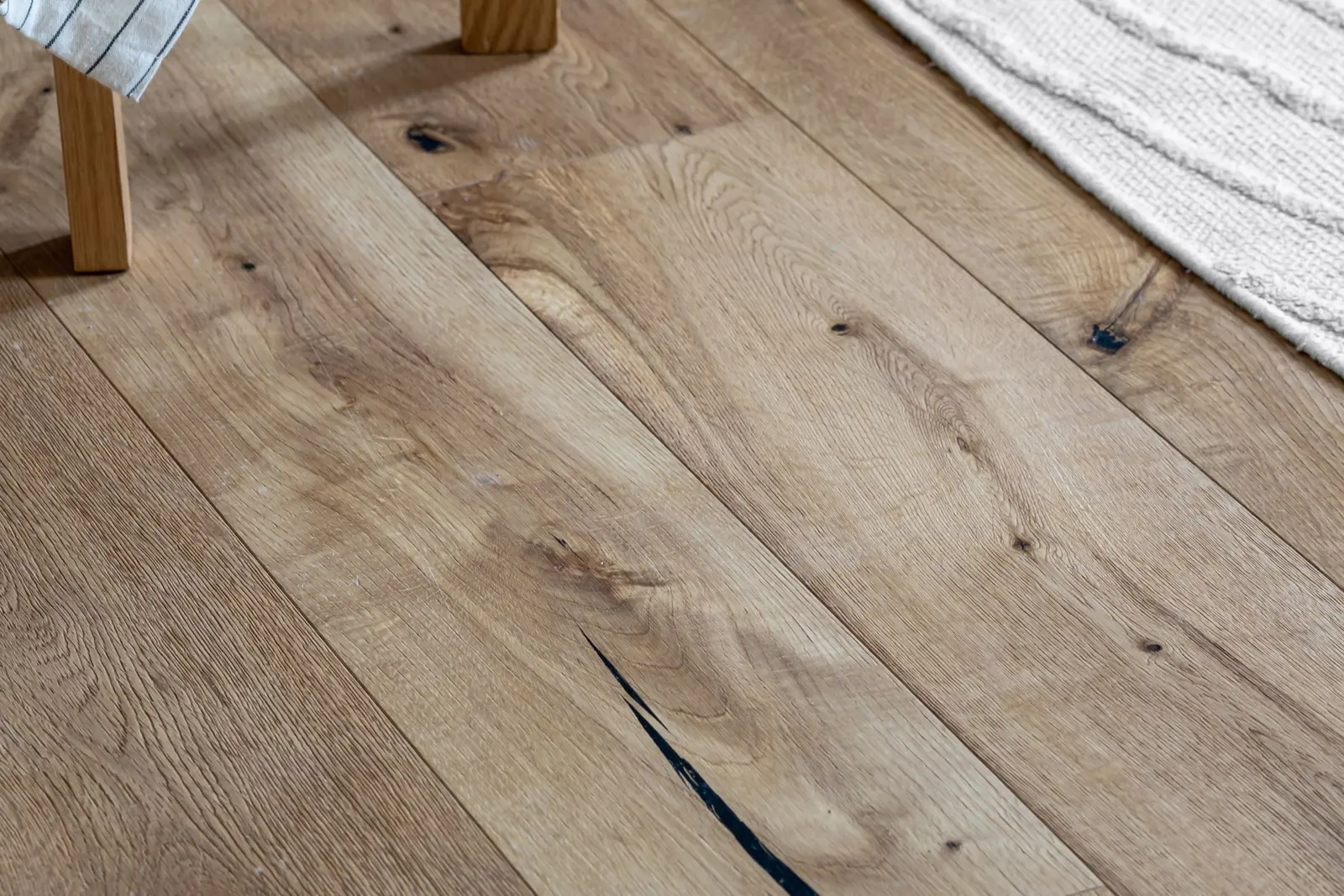 Close-up of wide light-oak plank flooring beside a woven rug and a timber table leg